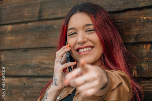 smiling young woman on the street using mobile phone and pointing finger photo