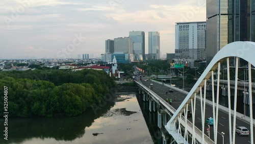 cars and motorbikes driving across modern bridge in PIK Jakarta at sunset photo
