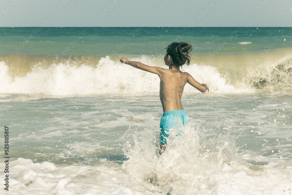 A little boy with long hair is playing in the waves of the sea. The boy was enjoying the waves of the sea.