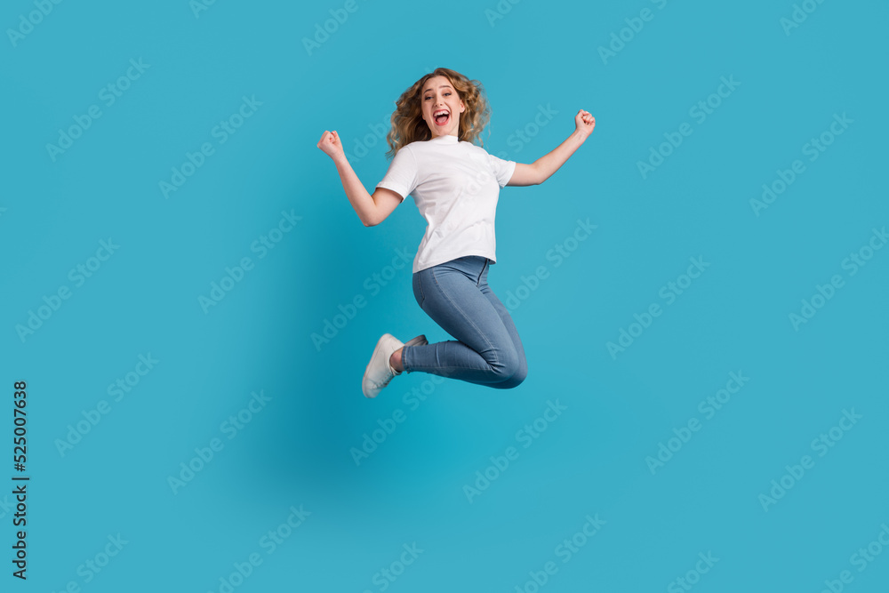Girl in white T-shirt and jeans jumping fist up victory on blue background