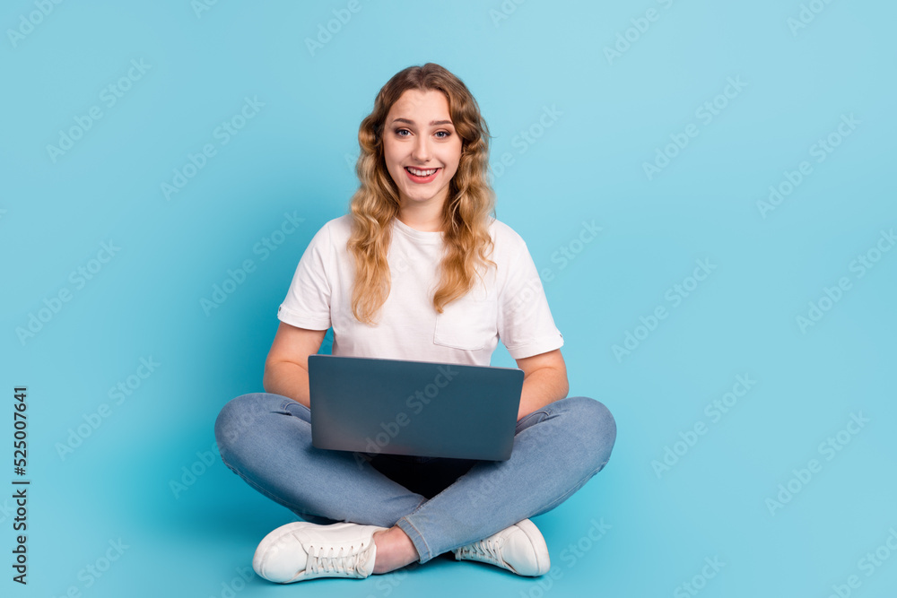 Image of young beautiful woman using laptop while sitting with legs crossed isolated over blue color background Image of young beautiful woman using laptop while sitting with legs crossed isolated over blue color background