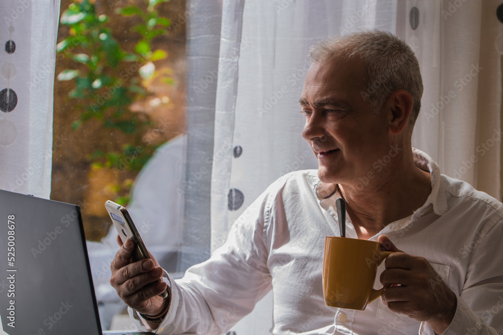 adult man working with pc and mobile phone while having breakfast at home adult man working with pc and mobile phone while having breakfast at home