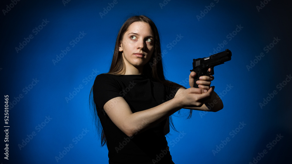 young beautiful woman with long hair in a black t-shirt with a gun on a blue background young beautiful woman with long hair in a black t-shirt with a gun on a blue background