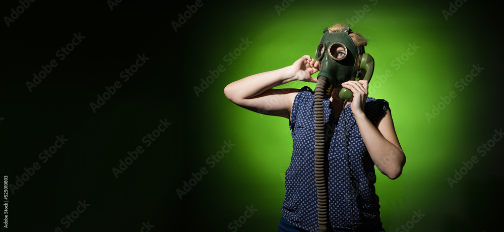 Funny woman in a gas mask calls on a retro phone on a dark background with copy space, hard light.