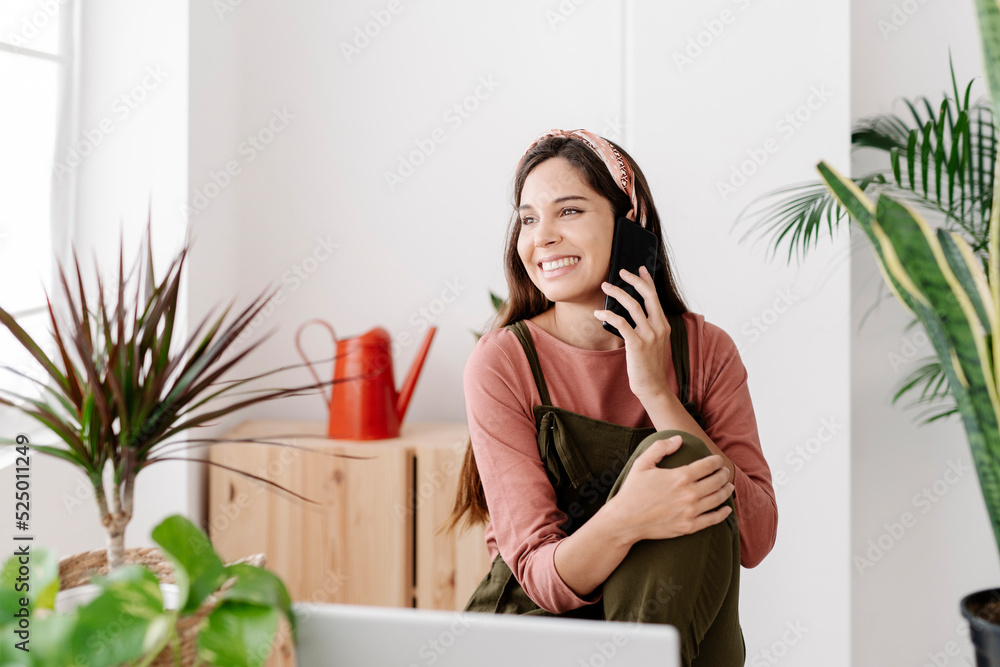 Smiling woman talking on phone sitting by potted plants at home Smiling woman talking on phone sitting by potted plants at home