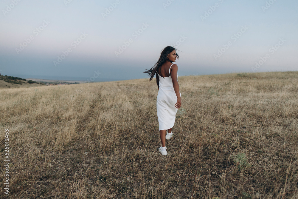 Woman wearing white dress walking in meadow in front of sky Woman wearing white dress walking in meadow in front of sky