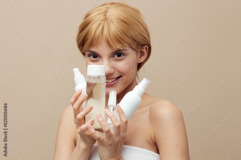 a sweet, young woman stands on a beige background holding various jars of cosmetics in her hands and hides her face from the camera behind them a sweet, young woman stands on a beige background holding various jars of cosmetics in her hands and hides her face from the camera behind them