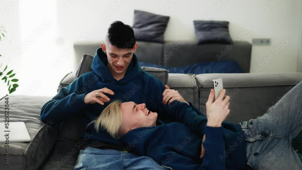 Happy men homosexual couple sit on sofa and using smartphone, talking Happy men homosexual couple sit on sofa and using smartphone, talking
