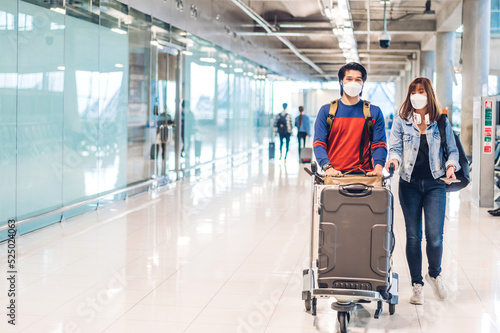 Young happy couple traveler in quarantine for coronavirus wearing surgical mask face protection hold passport and ticket before long travel vacation flight at International terminal airport