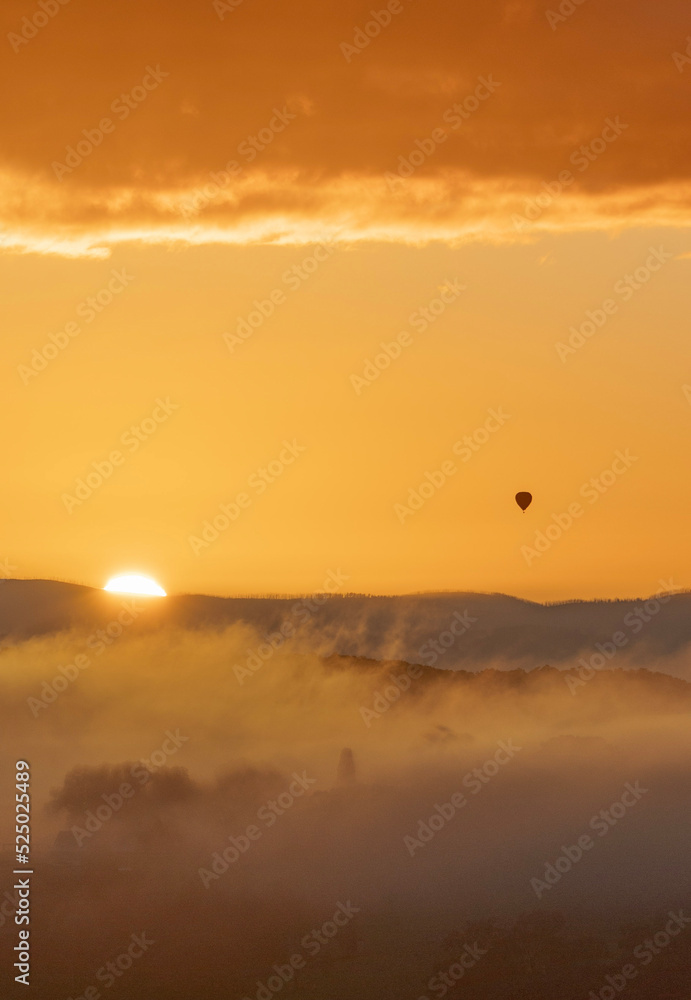 Golden sunrise with silhouette of a distant hot air balloon 