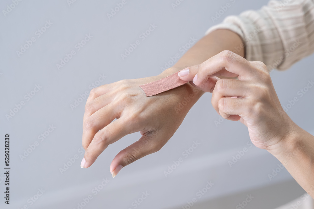 Young woman opens a band-aid, female sticking adhesive plaster bandage on her hand , closeup. medicine care Young woman opens a band-aid, female sticking adhesive plaster bandage on her hand , closeup. medicine care