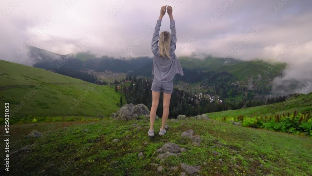 Young girl raised her hands up against background of clouds in high-altitude village in Georgian region of Bakhmaro. She is happy, beautiful view of sky and clouds. Delight overwhelms