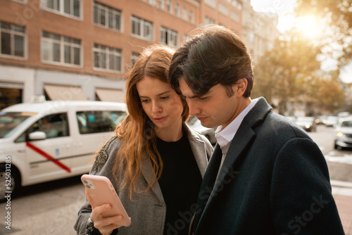 Loving young couple standing using smartphone on street