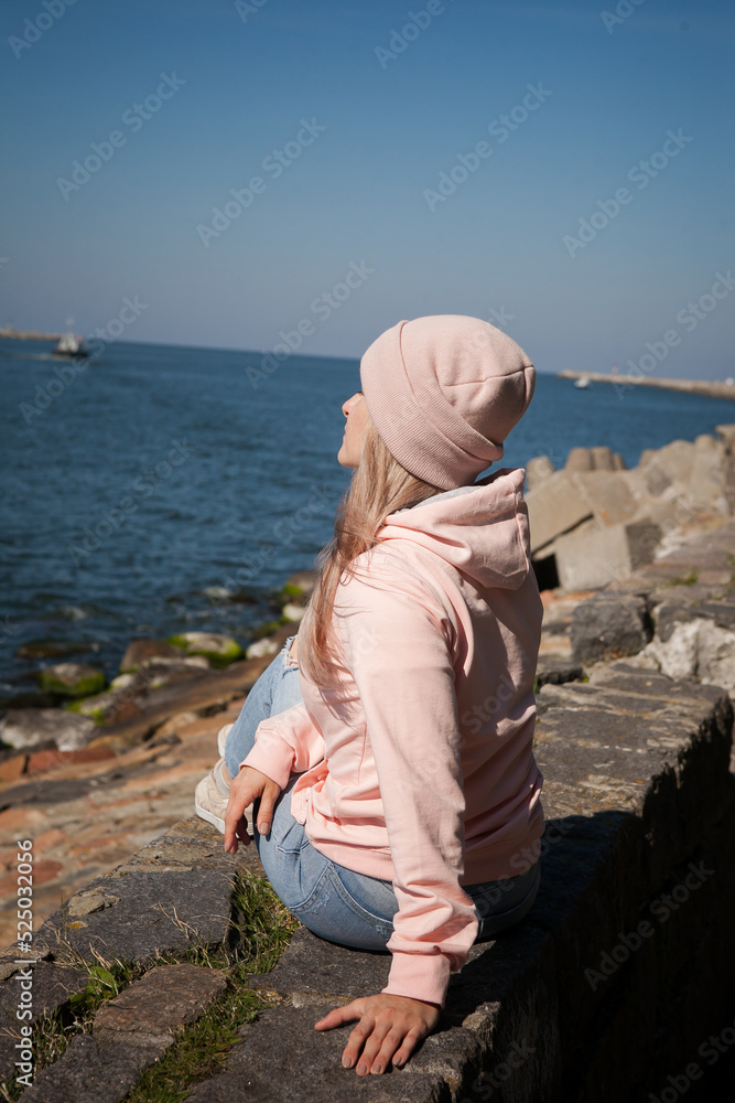 a blonde girl on the background of a cold sea, seagulls in the sky. travel and travel concept, immigration. girl pouring at the beach, casual outfit, backpacker, traveler