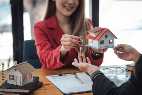 Real estate agent hand over the house key to customers after signing a real estate sales contract, handing over ownership. house and real estate trading idea.