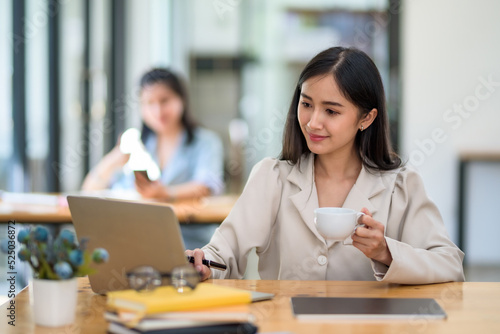 Beautiful Asian businesswoman using her laptop enjoys working, taking notes, reviewing assignments and enjoy reading.