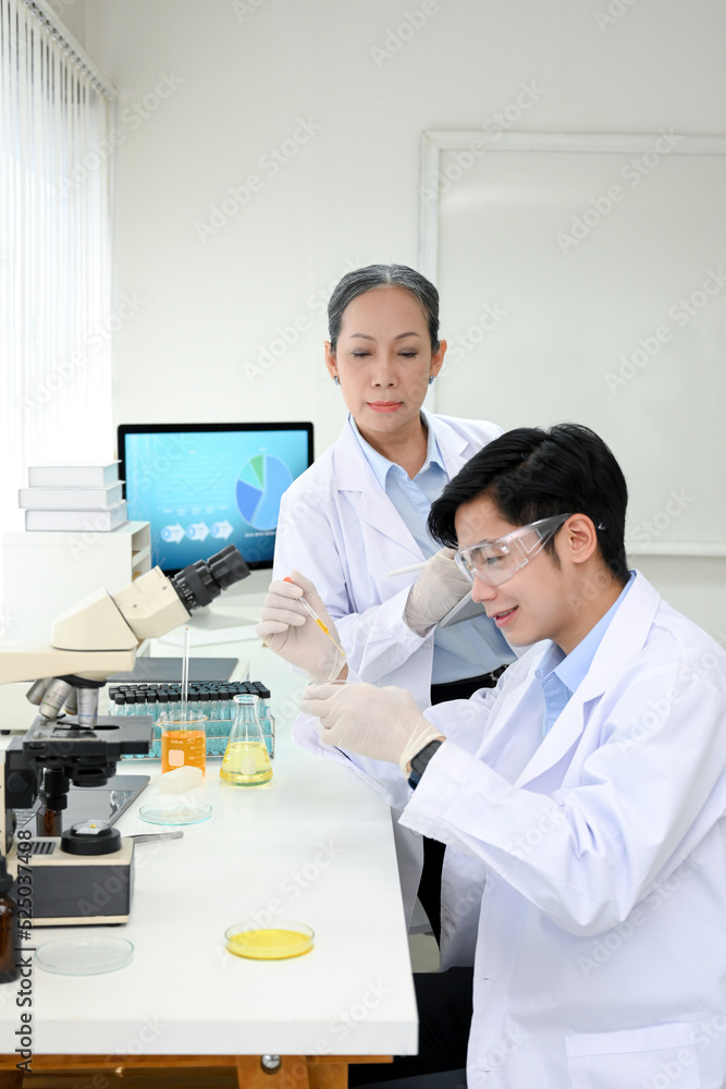 A professional Asian-aged female scientist instructs her new young male scientist in the lab