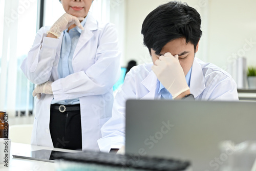 Unhappy Asian male scientist at his office desk, getting a complaint from his supervisor.