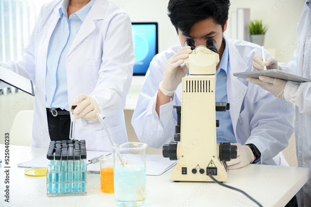 Asian male scientist examining virus specimen under a microscope in the