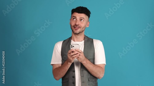 Happy brunet man wearing a vest and t-shirt texting by phone in the blue studio photo