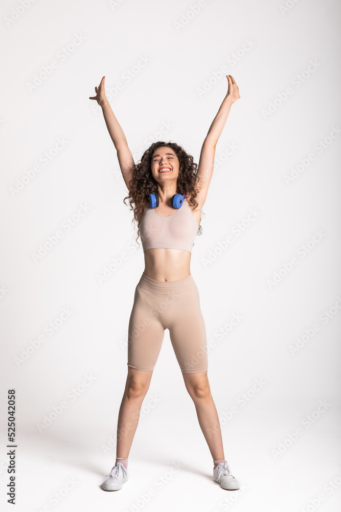 Fototapeta premium Full length portrait of a cheerful asian fitness woman in headphones working out isolated over white background