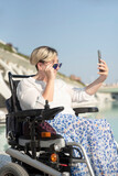 vertical portrait of smiling woman with disability in a wheelchair taking a selfie photo looking behind sunglasses