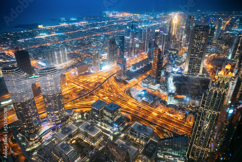 City background of illuminated cityscape with skyscrapers and modern urban architecture in Dubai resort town. Street night traffic in Dudai skyline. Waterfront and Dubai cityscape in evening