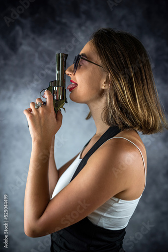 Young beautiful sexy brunette woman posing with a gun in her hand on a plain background.