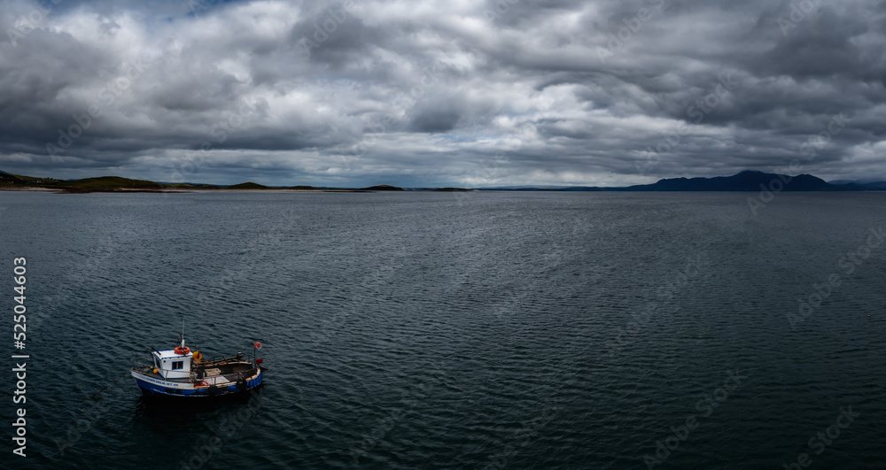single fishing boat in a deep blue ocean under a cloudy sky with coastal mountains in the background