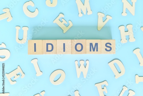 Idioms or idiom concept in English grammar class lesson. Wooden blocks typography flat lay in blue background. photo