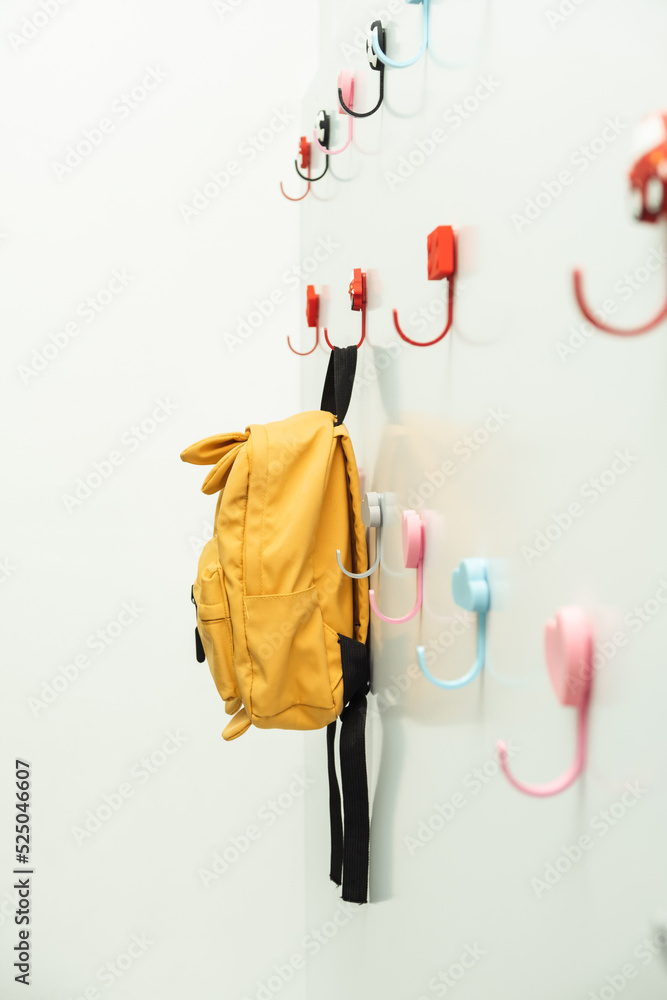 Cute yellow backpack hanging on a white hanger in the school locker