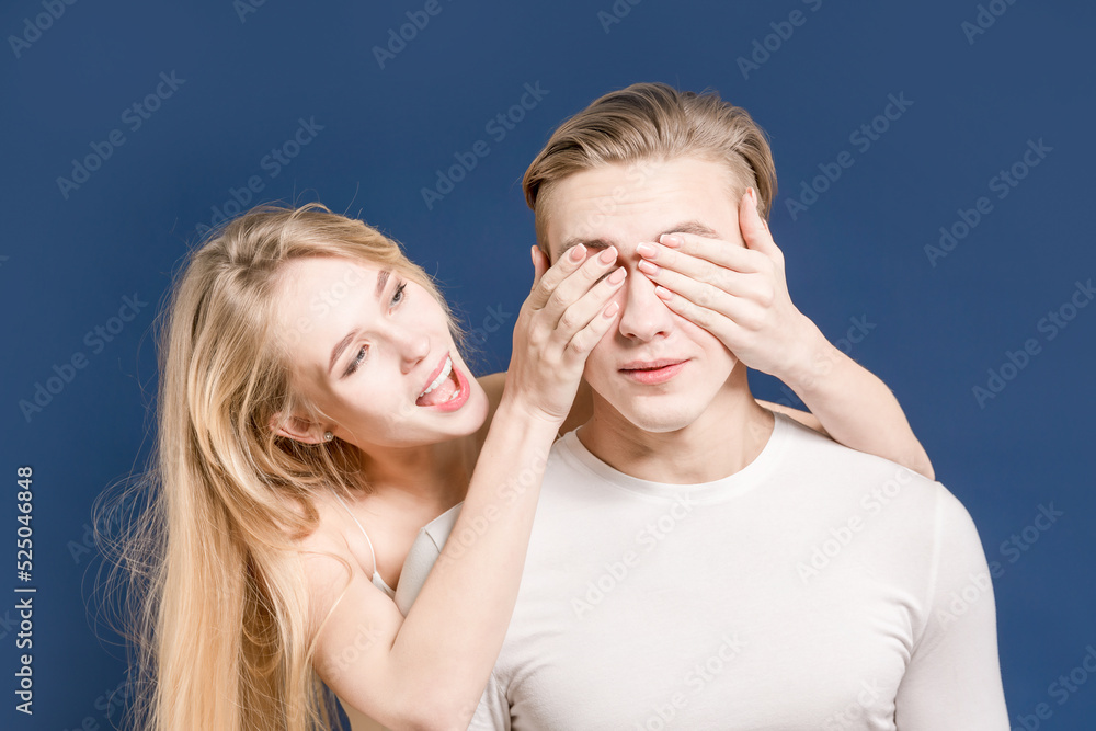 Young couple in the studio. The girl covers her eyes with a guy. Dark blue background. Young couple in the studio. The girl covers her eyes with a guy. Dark blue background.