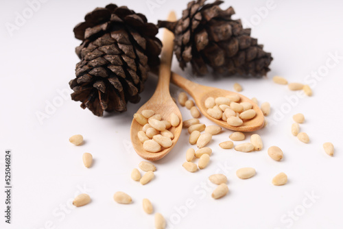 Heap of pine nuts and wood spoon and cedar cones on white background