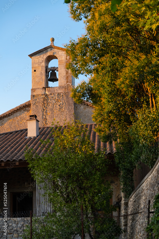 Church tower of a small chapel in Vallon Pont d’Arc village in southern France. Sunset atmosphere with warm evening light illuminating the bell tower in typical architecture of rural Provence region.