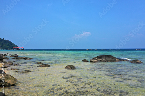 Tropical beach with stones and palm trees and a blue sea on Tioman Island in the South China Sea, belonging to Malaysia.