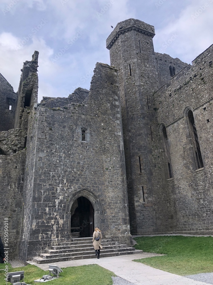Rock of Cashel with a tourist, County Tipperary, Ireland, spring 2022. Cashel of the Kings and St. Patrick's Rock, historic site, ruins of medieval castle and Cathedral. Top irish sightseeings
