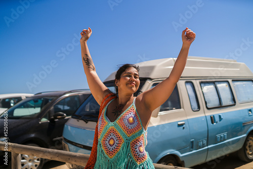 Chica joven guapa posando y sonriendo delante de furgoneta vintage en aparcamiento de la playa