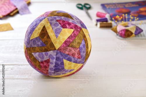 Patchwork ball made of pieces of fabric sewn in the shape of the letter Z on the background of quilting and sewing accessories