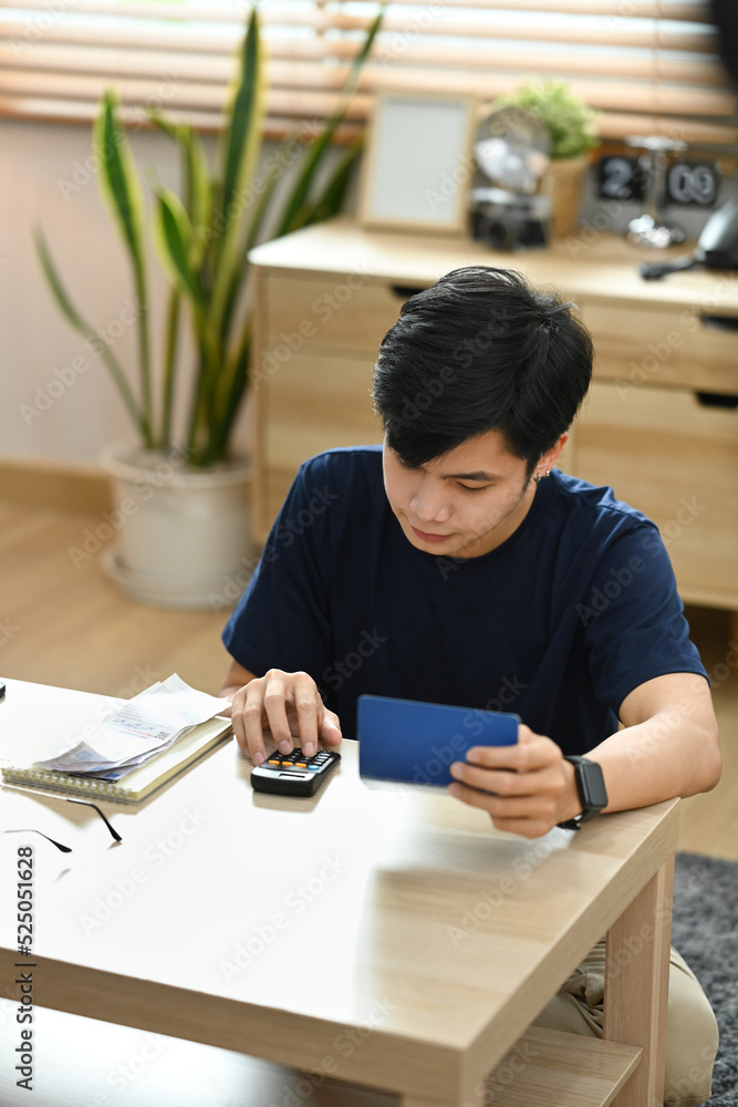 Focused man using calculator for calculating money bank loan rent payments, managing expenses finances in bright living room Focused man using calculator for calculating money bank loan rent payments, managing expenses finances in bright living room