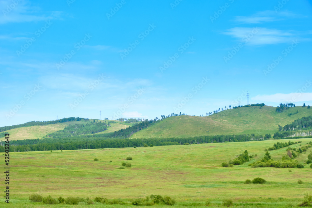 Green meadows of the Trans-Baikal Territory in Russia against a blue sky with clouds.