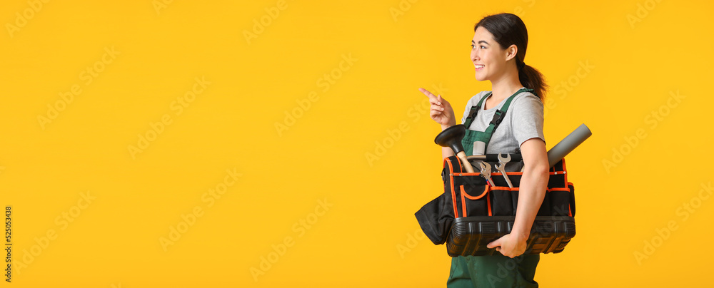 Fototapeta premium Female plumber with tools bag pointing at something on yellow background with space for text