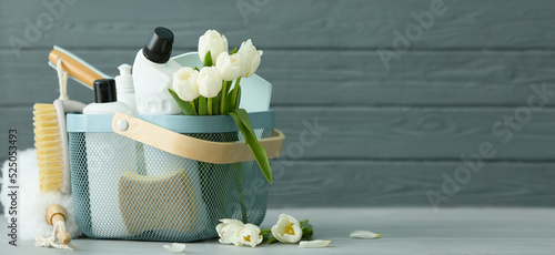 Set of cleaning supplies and spring flowers on grey wooden background