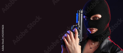 Fotografia Portrait of young woman in balaclava and with gun on dark background with space