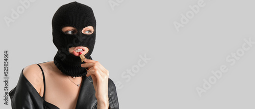 Young woman in balaclava and with lipstick on grey background with space for text