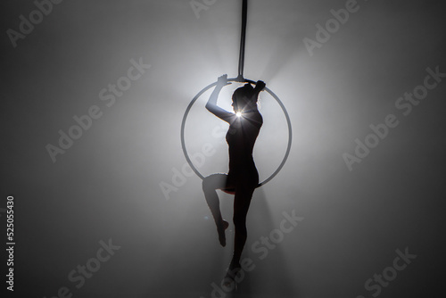 Konstfotografi Silhouette of flexible aerial gymnast on an aerial ring performs acrobatic tricks in the air