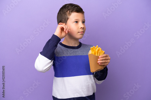 Little boy holding fried chips isolated on purple background having doubts and thinking