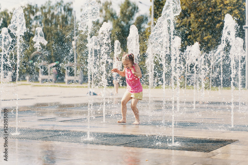 happy child playing with water splashes in city fountain