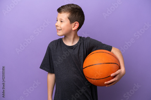 Little boy playing basketball isolated on purple background looking side