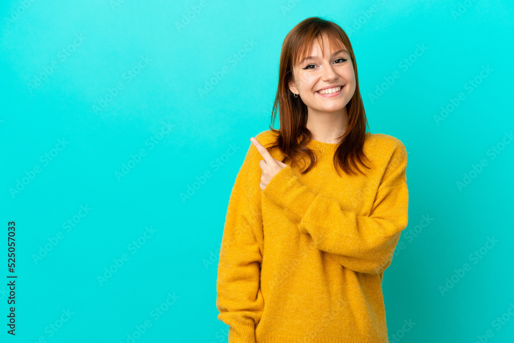 Fototapeta premium Redhead girl isolated on blue background pointing to the side to present a product