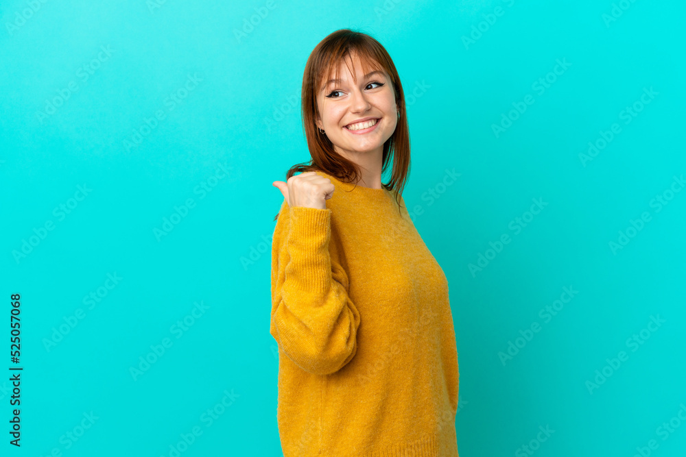 Redhead girl isolated on blue background pointing to the side to present a product Redhead girl isolated on blue background pointing to the side to present a product